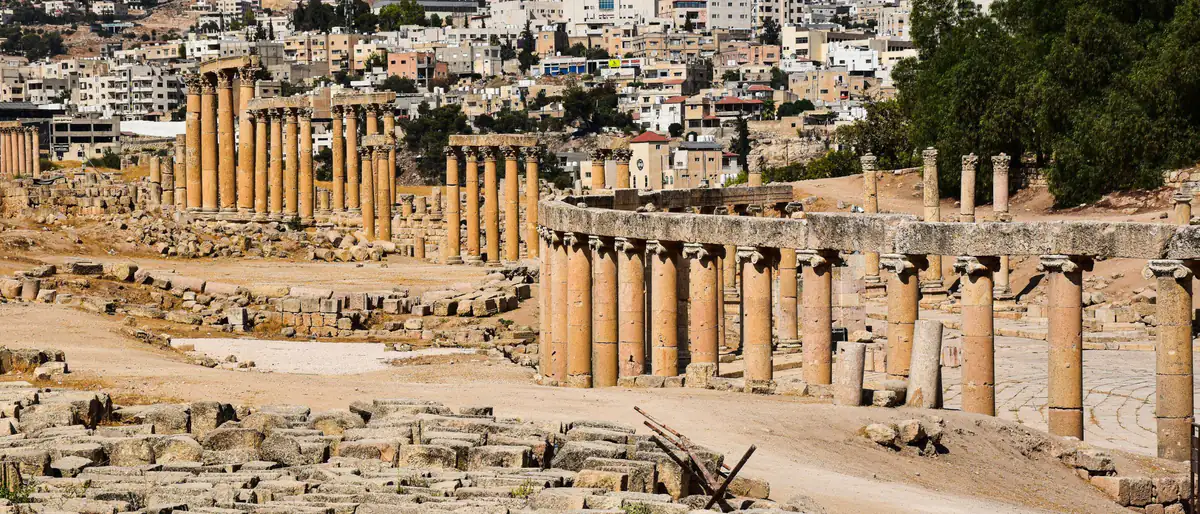 مواقيت الصلاة في جرش: أعمدة الساحة البيضاوية الأثرية في جرش، وخلفها بيوت مدينة جرش الحديثة